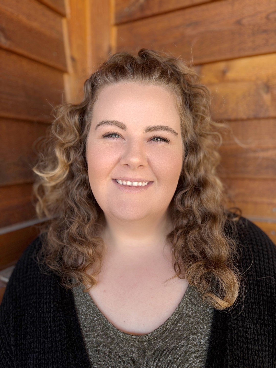 Person smiling with curly hair, wooden background.