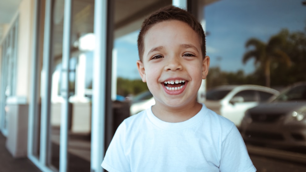 Smiling child outdoors with parked cars background.
