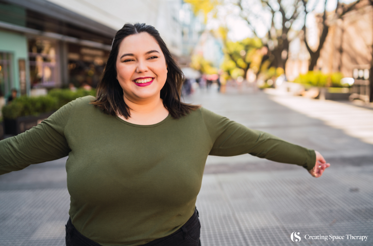 Plus-size woman in a green shirt smiling warmly with arms wide open, expressing joy and openness.