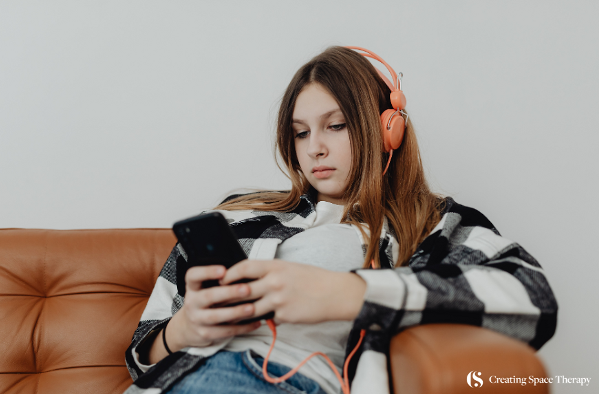 Teen girl looking at phone while lounging on sofa.