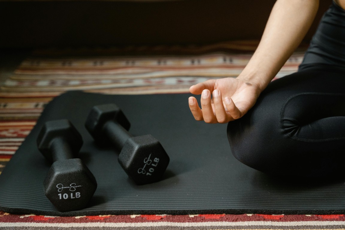 Person meditating near dumbbells on yoga mat